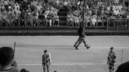 Wagah border, Amritsar, India - September 2016: Black and white street photograph of Indian army Soldiers doing parade during Wagah-Attari border ceremony with crowd watching them from their seatsのeditorial素材
