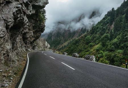 An empty road with green mountains and clouds by the sideの写真素材
