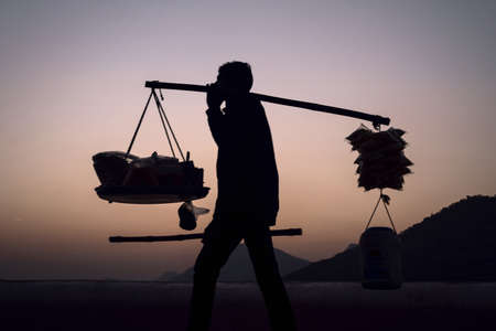 Silhouette of a street vendor carrying everything on his shoulder during sunset in Udaipur, Rajasthanの写真素材