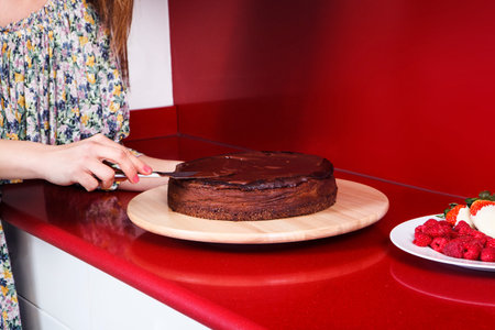woman's hands putting the chocolate base to a cheesecake in a red kitchenの写真素材