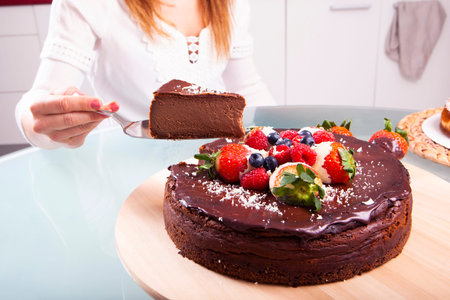 Woman's hands with pink nails serving a slice of chocolate cheesecake with strawberries, blackberries and blueberriesの写真素材