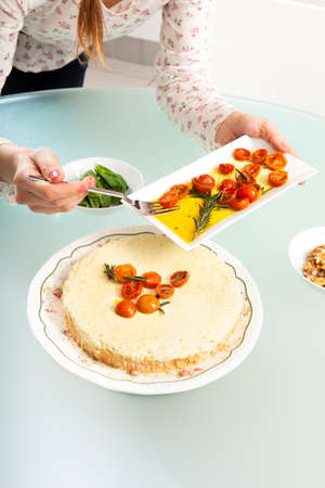 Close-up of the girl's hands decorating pesto cheesecake with cherry tomatoesの写真素材