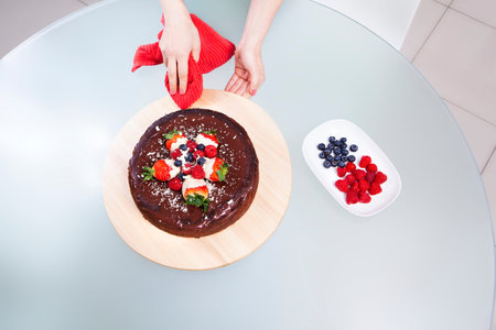 Woman preparing chocolate cheesecake with strawberries. Cleaning the base with a red cloth.の写真素材