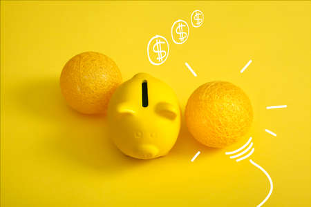 piggy bank with light bulb and drawn coins, saving idea concept. Vivid yellow background.の写真素材