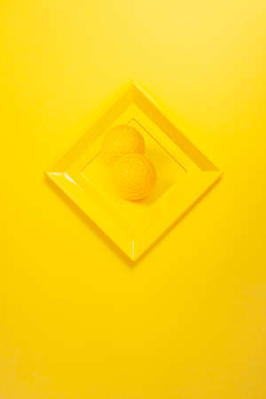 modern yellow photo frame on yellow wall in the shape of a diamond, with a photo of two yellow balls. Copy space.の写真素材