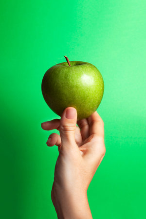 female hand holding a green apple with green background and copy space