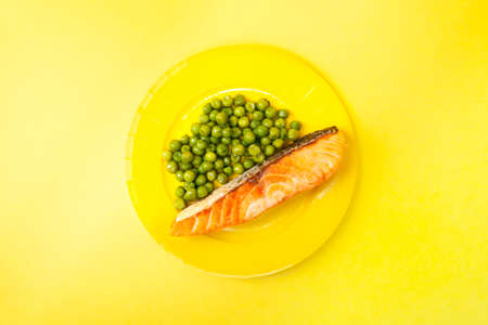 Homemade grilled Salmon dish with peas on yellow plate and yellow backgroundの写真素材