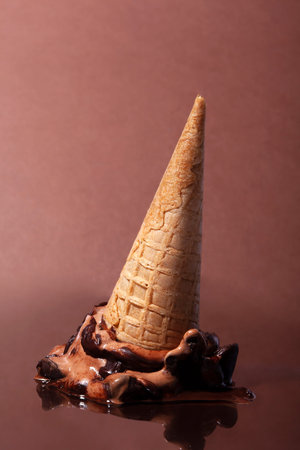 melted upside down chocolate cone ice cream on a brown background with copy space