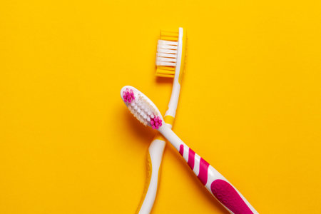 2 color pink and yellow toothbrushes with yellow background. Copy spce.