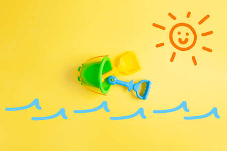 summer scene with a mixture of drawing of sun and sea waves and photography of a children's bucket. Vacation scene on the beach. Summer time concept.の写真素材