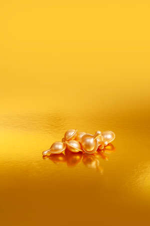 Close-up of golden capsules for cosmetic treatments on golden backgroundの写真素材