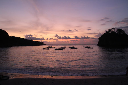 Colorful sunset in Nusa Penida, Bali. Purple, pink and orange colors. Water, boats and islands. Sunset reflection in the ocean. Sunshine through the clouds. Island holidays.の写真素材
