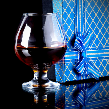Glass with alcohol and a gift. Alcohol and gift box. Box with a bow and glass with drink.の写真素材