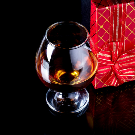 Glass with alcohol and a gift. Alcohol and gift box. Box with a bow and glass with drink.の写真素材