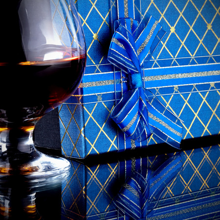 Glass with alcohol and a gift. Alcohol and gift box. Box with a bow and glass with drink.の写真素材