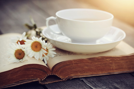 White porcelain cup, camomiles and the open old book on a wooden tableの写真素材