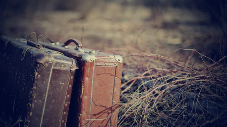 Two old shabby suitcases, stand forgotten on the road in a faded grass.の写真素材