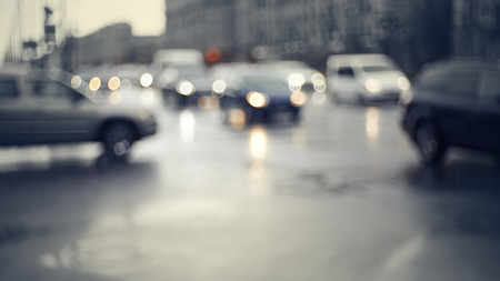 Blurry unfocused background with the city road with cars in twilight after a rain. Out of focus city landscape in twilight after a rain.の写真素材