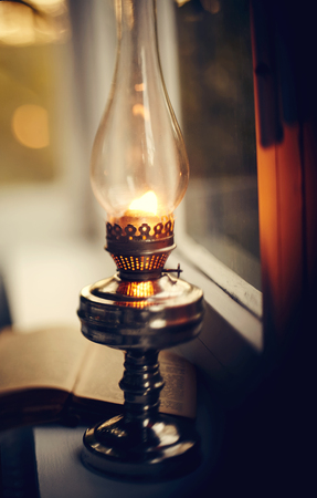 Vintage kerosene lamp stands on a white windowsill in the eveningの写真素材