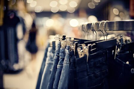 Jeans on the hanger in the store. Clothes on hangers in shop for sale. Blur background. Fashionable clothes in a boutique. Various clothing on market.の写真素材