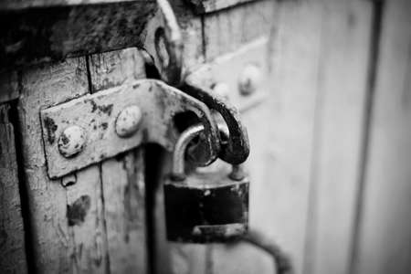 A rusty old lock on a old wooden door. A gate closed on the lock. Not color image.の写真素材