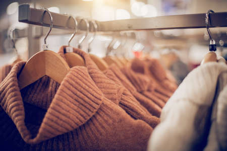 Sweaters on hangers. Shopping in store. Clothes on hangers in shop for sale. Blur background. Fashionable clothes in a boutique. Various clothing on market.の写真素材