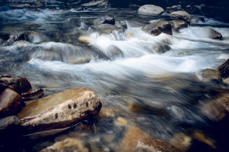 The rapid flow of the river with a rocky bottom. Background with water flowing over the stones.