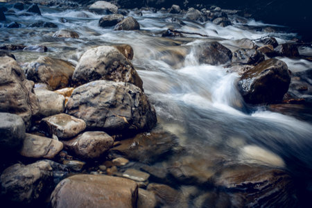 The rapid flow of the river with a rocky bottom. Background with water flowing over the stones.