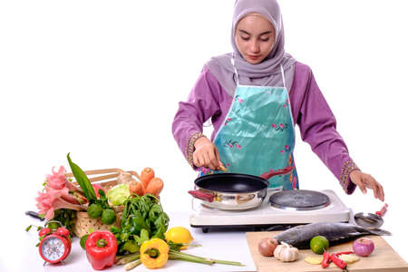 Beautiful young woman with green apron cooking home against white background.の写真素材