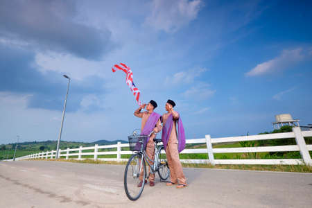 Muadzam Shah, Malaysia - July 21st, 2017 : Young stylish handsome twins with old bicycle  at First Dairy Farm , Muadzam Shah  holding and giving a  salute to Malaysian flag. Independence Day Concept .のeditorial素材
