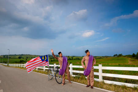 Muadzam Shah, Malaysia - July 21st, 2017 : Young stylish handsome twins with old bicycle standing on the road at First Dairy Farm , Muadzam Shah  holding a Malaysian flag. Independence Day Concept .のeditorial素材