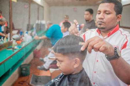 Muadzam Shah, Malaysia - August 14th, 2017 : Little boy getting warber while sitting haircut on chair at barbershop.のeditorial素材