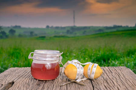 Fresh organic honey in glass jar , measuring tape , lemon and alarm clock on old wooden with blurred background ,healthy nutrition,strengthening immunity, diet and treatment of fluの写真素材