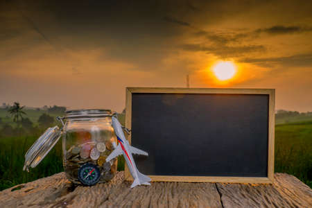 Saving planning for Travel budget of holiday concept,Financial, coins money in the jar, compass and airplane wooden table with sunrise backgroundの写真素材
