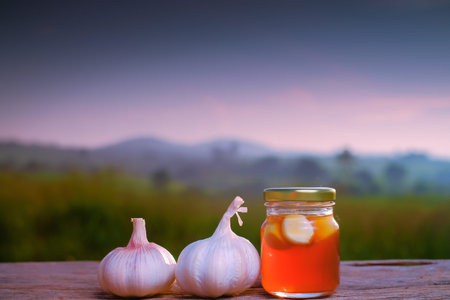 Fresh honey in a jar and garlic on old wooden table with nature background. Natural medicineの写真素材
