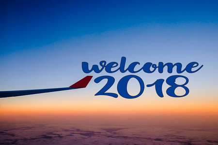 Welcome 2018 : Wing of an airplane flying above the clouds at sunsetの写真素材