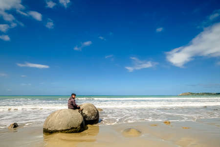 Moeraki, New Zealand â Desember 18th,  2017. A young boy posing on the unusual spherical Moeraki Boulders which are found on Koekohe Beach on the Otago Coast of New Zealand's South Island.のeditorial素材
