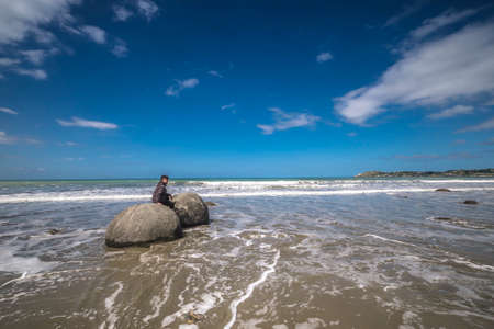 Moeraki, New Zealand â Desember 18th,  2017. A young boy posing on the unusual spherical Moeraki Boulders which are found on Koekohe Beach on the Otago Coast of New Zealand's South Island.のeditorial素材
