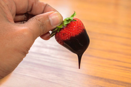 Man hands holding fresh strawberry dipped in chocolate sauce on a wooden tableの写真素材