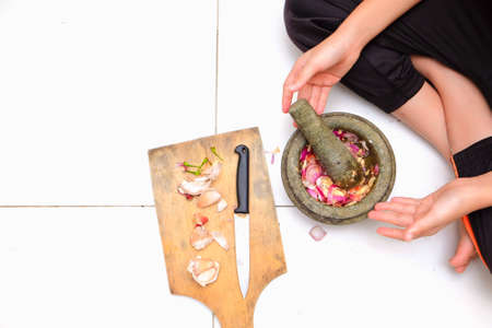 An Asian boy  is using the mortar and pestle or lesung batu in Malay with crushed chilies, onions and garlic for cooking rice friedの写真素材