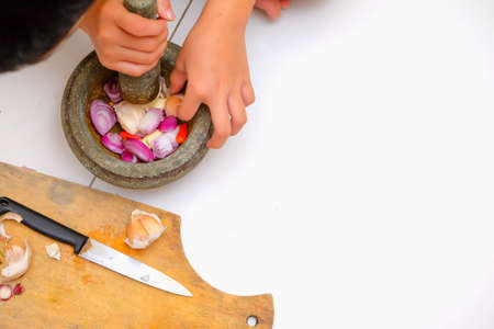An Asian boy  is using the mortar and pestle or lesung batu in Malay with crushed chilies, onions and garlic for cooking rice friedの写真素材