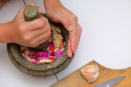 An Asian boy  is using the mortar and pestle or lesung batu in Malay with crushed chilies, onions and garlic for cooking rice friedの写真素材