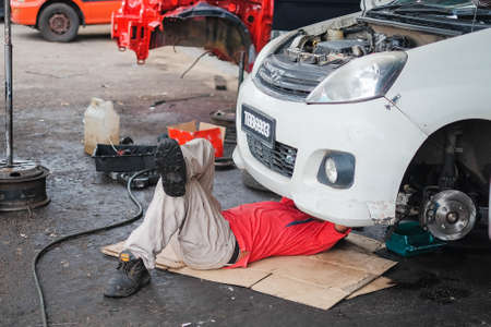 Muadzam Shah , Malaysia - December 28th, 2017 :  Mechanic in red shirt  lying down and working under car at auto service garageのeditorial素材