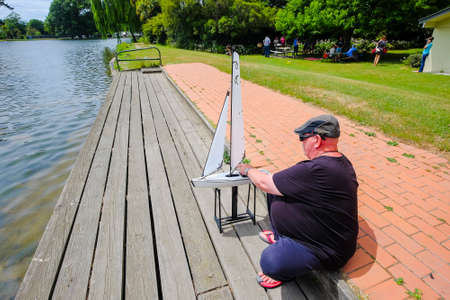Christchurch, New Zealand  December 18th, 2017 : Senior man with radio controlled model sailboat on lake being launched by senior citizen  in Christchurch Botanic Garden , New Zealand.のeditorial素材