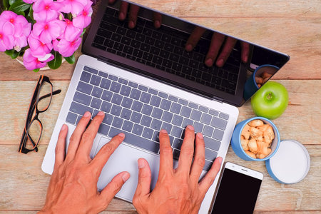 Business workplace from the top, flay lay.Hand on a laptop, an apple, smartphone, glasses, plant,...
