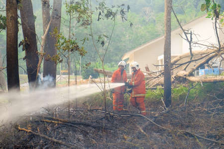 Muadzam Shah, Malaysia - May 7th, 2018: Two firemen wearing safety helmet spraying water to fire surround with smoke and dust in the bush fire.のeditorial素材