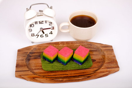 Traditional Malaysian food. Kuih Lapis , alarm clock and  a cup of coffee isolated on white...