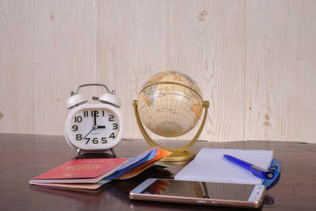 Accessories of travel concept with note book, globe, passport, money , smartphone and alarm clock on wooden backgroundの写真素材