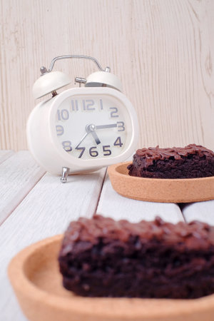 Alarm clock and chocolate brownie with melted chocolate on a wooden plate