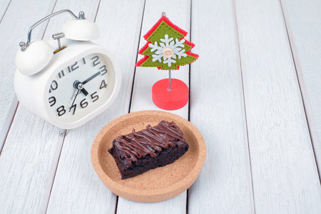 Alarm clock, note clipper and  chocolate brownie with melted chocolate on a wooden plate